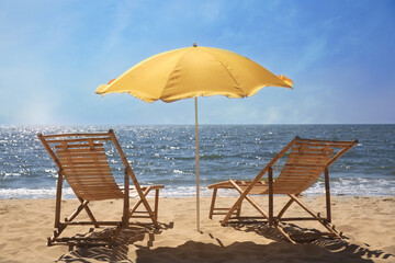 Orange beach umbrella and deck chairs on sandy seashore