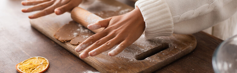 Obraz na płótnie Canvas Cropped view of african american woman rolling dough near dry orange slice in kitchen, banner