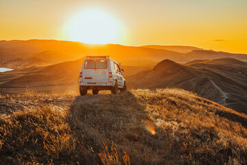 The jeep is standing on the top of the mountain in the sunset. A delightful landscape and the concept of travel, freedom and adventure