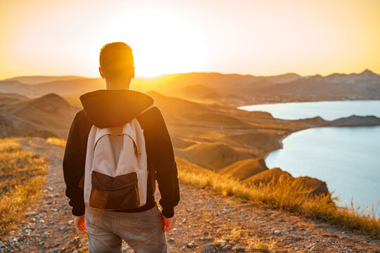 A young man travels along the mountain coast at sunset. Rear view A man stands on a mountainside and enjoys the view. The concept of freedom and relax