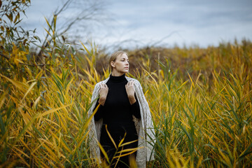 girl in black golf with a gray cape on her shoulders among the tall grass