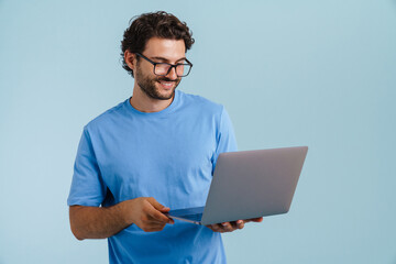 Young brunette man in eyeglasses smiling while using laptop