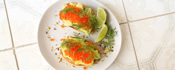 plate with bruschettas with avocado and red caviar on a light table