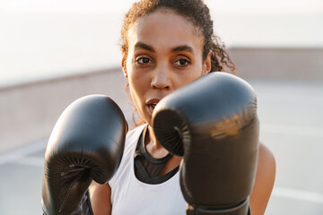 Black sportswoman boxing while working out on parking