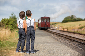 Obraz premium Beautiful children, dressed in vintage clothes, enjoying old steam train on a hot summer day