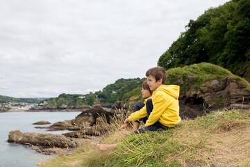 Naklejka na ściany i meble Children, enjoying quiet cloudy day on the ocean shore on the cliff, rocky beach