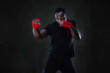 Sporty man during boxing hit. African american muscular athlete in sport uniform and red bandage...
