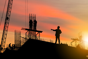 Silhouette of Engineer and worker on building site, construction site at sunset in evening time
