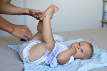 Mother putting diaper on her happy baby in nursery.
