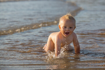 Baby boy, playing on the beach in the water, smiling