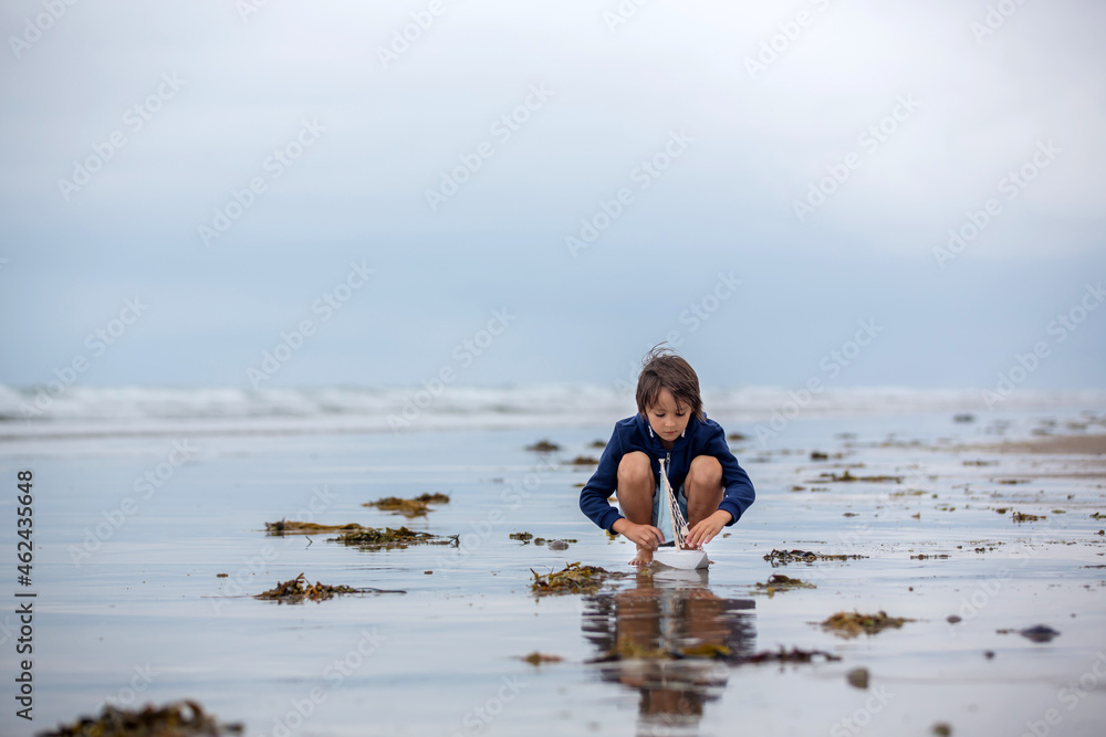 Sticker Child plays with sand on beach. Cute preschool boy with toy ship on beach. Stormy seaside sgore and kid playing