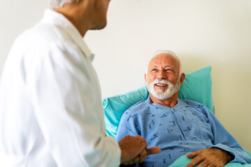 Doctor talking to senior male patient in hospital bed who is recovering from the disease