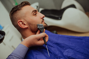 The barber paints the beard and the mustache of the young man in the barbershop.Selective focus