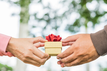 Hands couple holding packaged present together. Hands female and male holding a gift wrapped with ribbon in park for Birthday, Christmas, New year, Valentine's, Graduate, Celebrate.