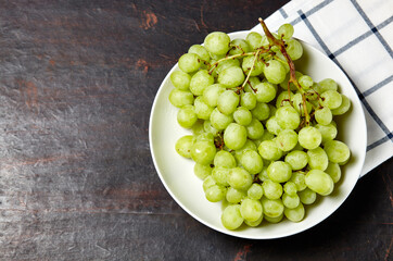 Branch of ripe green grape on plate with water drops. Juicy grapes on wooden background, closeup. Grapes on dark kitchen table with copy space