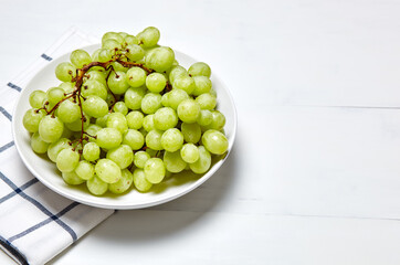 Branch of ripe green grape on plate with water drops. Juicy grapes on wooden background, closeup. Grapes on white kitchen table with copy space