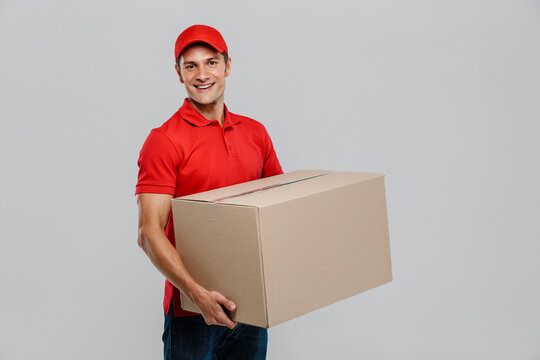 Young delivery man in hat smiling while posing with cardboard box