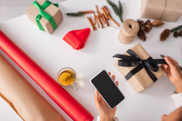 Top view of african american woman holding smartphone while decorating christmas gift at home
