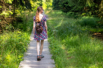 on a hike - a young woman in a summer dress walking on a wooden path in the forest