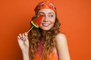 Young ginger woman wearing bandana smiling while posing with lollipop