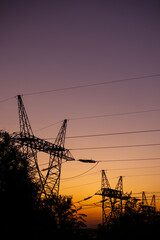 Silhouettes of high voltage pylons against the orange sky during sunset. Photo taken at dusk under natural lighting conditions