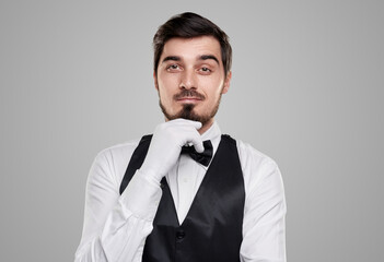 Confident waiter touching chin on gray background