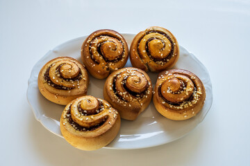 Freshly baked cinnamon rolls with spices and cocoa filling on a white serving plate over white background. Selective focus.