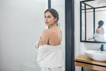 A young woman in a white robe with one shoulder naked in the bathroom
