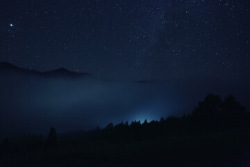 Picturesque view of night sky with beautiful stars over foggy hill