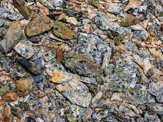 Multicolored detailed texture of a rocky mountain slope. Geological scattering of stones in close-up. Nature background of chaotic pile of stones. Minimalist texture of stony heap
