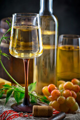 White wine in a bottle and glass on a background of an oak barrel and grapes