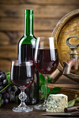 Red wine in a bottle and glass against the background of an oak barrel and grapes.
