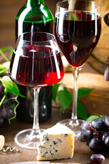 Red wine in a bottle and glass against the background of an oak barrel and grapes.