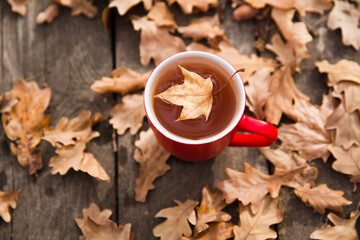 red mug with tea on an autumn wooden table with fallen leaves. Hello autumn morning.