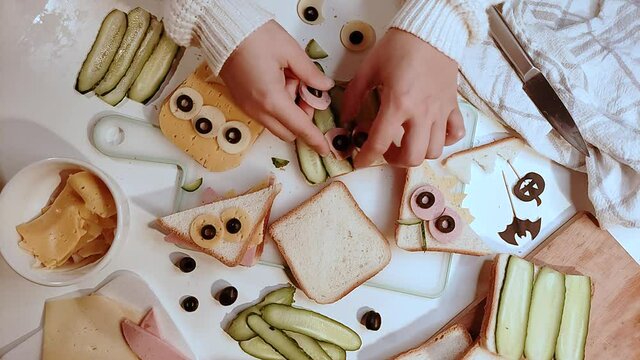 Various funny monster Halloween sandwiches. Cooking creative breakfast snack toasts with cheese, Halloween kids party food, mother woman hands in picture top view
