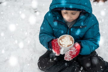 Little boy in drinking hot cocoa in the snow
