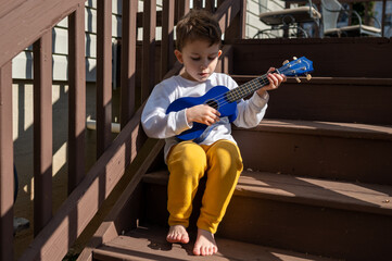 Little boy playing the ukulele in the sunshine