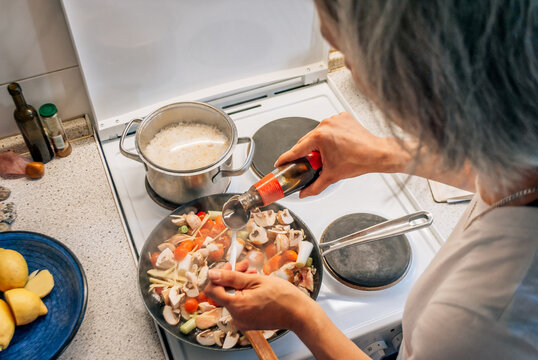 Woman pours oyster sauce into frying pan with vegetables and mushrooms