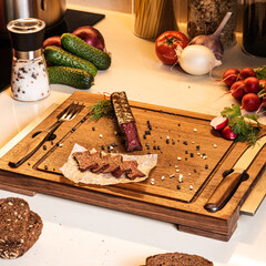 Ingredients for light snack. Cured sausage served on a wooden board with pepper, salt and bread - 462451089