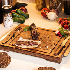 Dry-cured hourse sausage on a wooden board among fresh vegetables and bread on the kitchen table. Breakfast ingredients