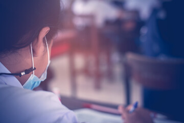 Uniform student taking exam while wearing face mask due to coronavirus emergency. Young woman sitting in class with wearing surgical mask due to Covid-19 pandemic