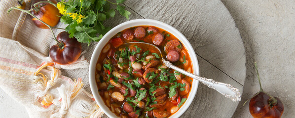 bowl of tomato and bean soup with smoked sausages on the table