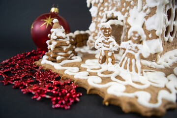 Pair of gingerbread men against backdrop of homemade gingerbread house painted with white sweet icing on black background.