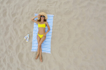 Woman sunbathing on beach towel at sandy coast, aerial view. Space for text