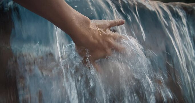 Close up soft movement of female hand touches the water in waterfall. Calm on the fresh air with water drops on national park. Clear and pure nature feeling good.