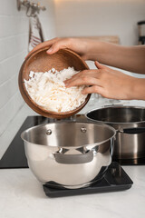 Woman pouring wax flakes into pot on scale in kitchen, closeup. Making homemade candles