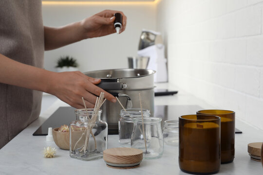 Woman Adding Essential Oil Into Pot With Melted Wax On Stove In Kitchen, Closeup. Making Homemade Candles