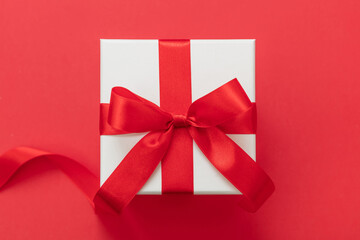 Gift box red ribbon and bow on red background, Christmas present satin curly decoration,