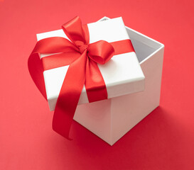 Gift box red ribbon and bow on red background, Christmas present satin curly decoration,