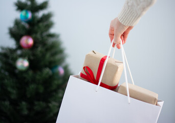 close-up of the hands of a young women carrying a paper bag full of gift boxes decorated with a red...